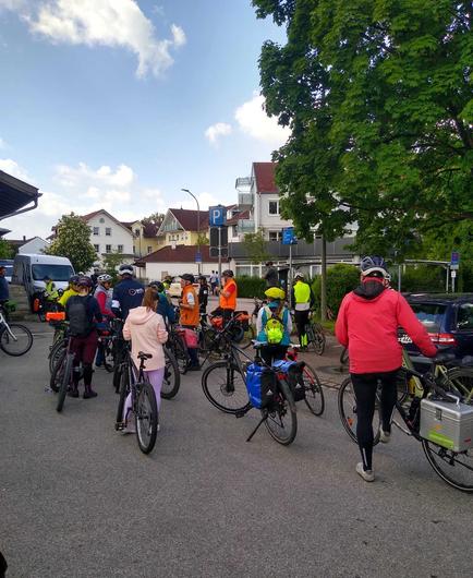 diverse Radler am Bahnhof in Wolfratshausen, rechts ein oder Bäume, der Himmel ist blau mit einigen Wölkchen