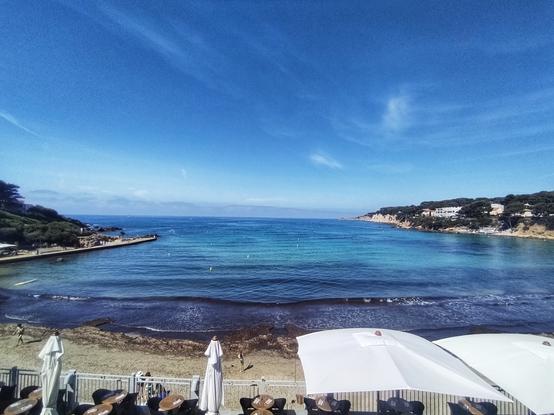 Plage et baie de Portissol depuis au dessus de la terrasse d'un restaurant avec parassol. Plage en forme de U orientée vers ouest entre la pointe de Portissol (à gauche) et la pointe de la Cride (à droite)