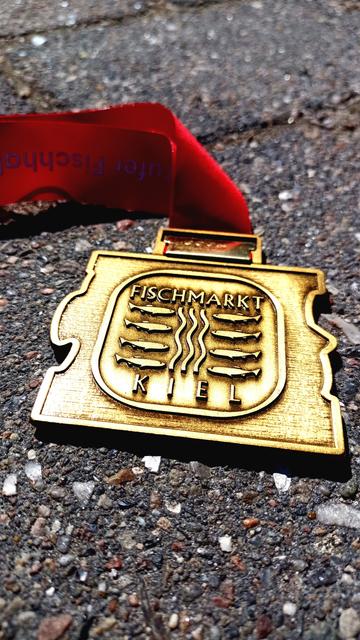 Eine bronce-farbene Medaille mit der Aufschrift "Fischmarkt" an einem roten Band.