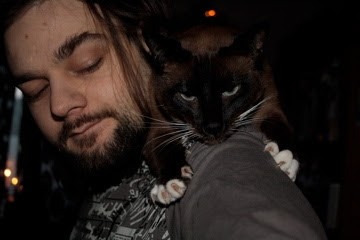 Shiva the Cat stretched out across FiXato's shoulders, with her claws dug into his left shoulder.
FiXato looking at her with an expression of "what are you doing, dear?"