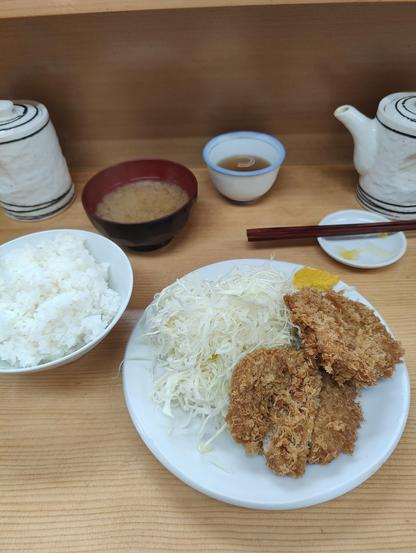 A photo of a Tonkatsu meal set. You see deep fried breaded pork, shredded cabbage, rice, and miso soup