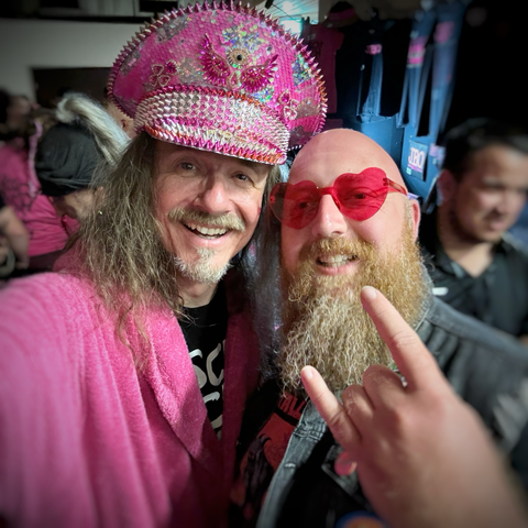 Vito mit JBO-Fan. Vito trägt eine über und über pink verzierte Kappe. Der Fan macht das Metal-Symbol mit der Hand.