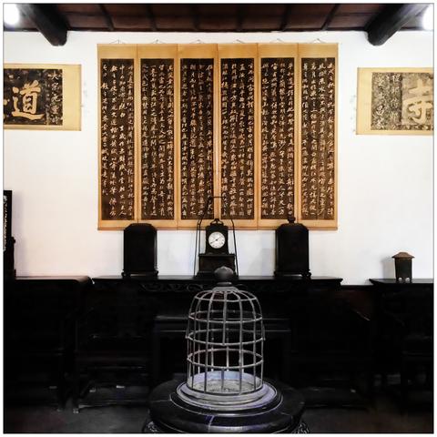 A room with antique furniture, a ceremonial fireplace, a clock, and Chinese calligraphy hanging on the wall.