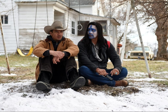 Twee mannen zitten naast elkaar op de grond vlakbij een speeltoestel met schommels. De één heeft een cowboyhoed op, de ander z'n gezicht geschilderd en een revolver in zijn hand.