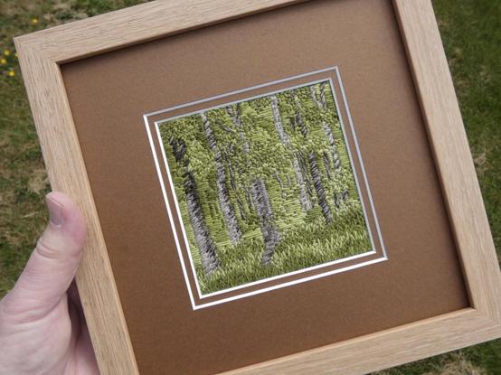 The framed artwork held in the artist's hand for scale. Frame is roughly 8x8 inch
