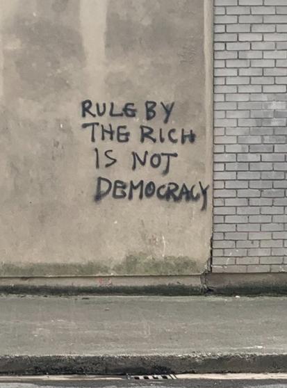 Foto Hauswand mit Graffiti:
Rule by the rich is not democracy
(Die Herrschaft der Reichen ist nicht Demokratie)