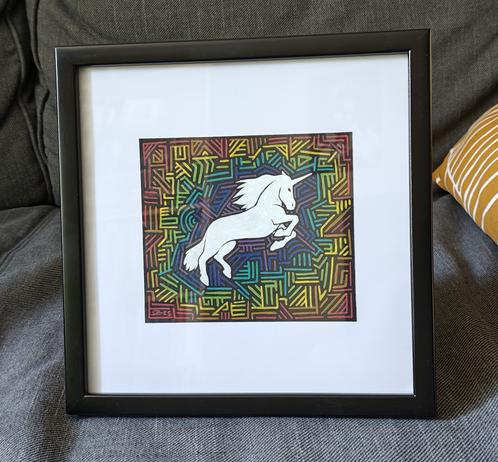 Framed artwork of a jumping white unicorn silhouette surrounded by random geometric lines in rainbow colors. Starting in the middle around the unicorn with purple and blue and ending at the edge with red and orange