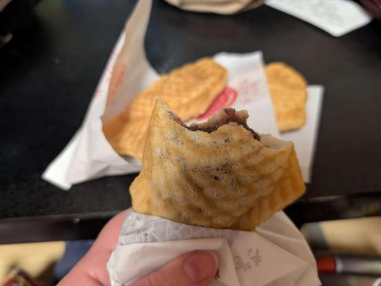 A photo of a half -eaten taiyaki, which is a fish shaped waffle confection filled with delicious stuffs. Two more uneaten taiyaki sit waiting on a table
