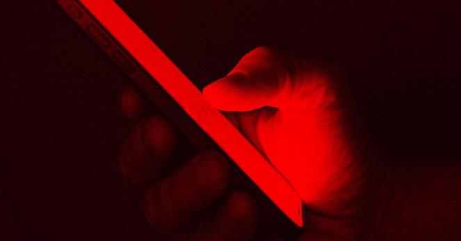 hand with smart phone lit by red light