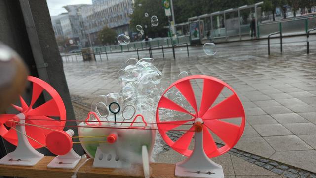 Die Maschine in Nahaufnahme wie sie Seifenblasen in den Regen pustet.