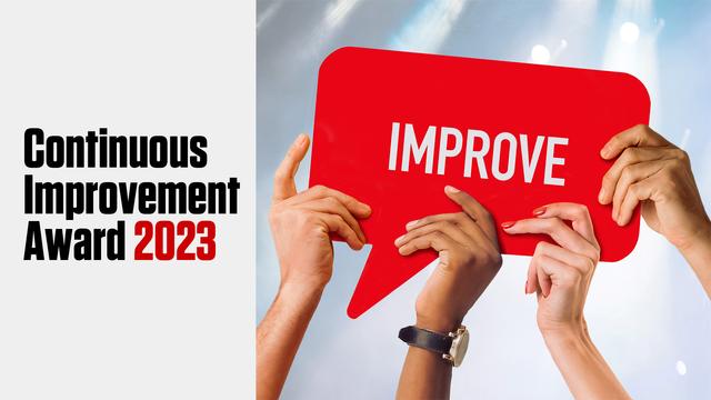 The banner from the previous continuous improvement award in 2023. Four hands are holding a sign on which is written "IMPROVE"