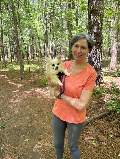 Woman in orange tshirt smiling and holding a tan long-haired chihuahua