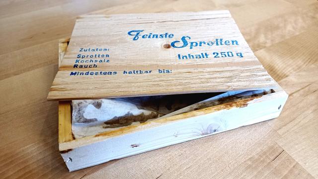 Ein geöffnete Holzkiste Kieler Sprotten liegt auf einem Holztisch.