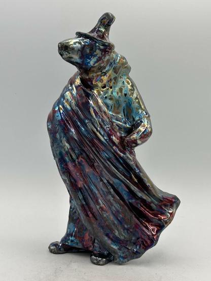 A raku bear sculpture in a witches hat and robe that has been raku fired.  The glaze is iridescent and multicoloured.