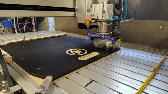 Holzplatte liegt auf CNC Fräse, eine Winkekatze wird eingefräst.