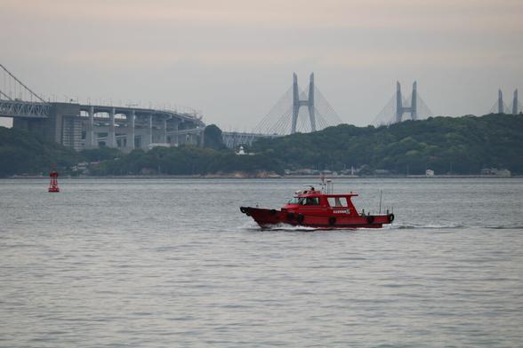 A small red boat in the Seto Inland Sea. There's the Great Seto Bridge and Yoshima in the background.
