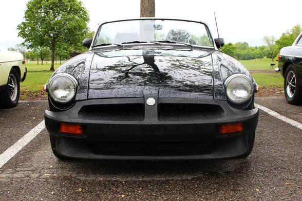 Photo of the front end of a black 1976 MG MGB on a rainy day in the parking lot of a park.