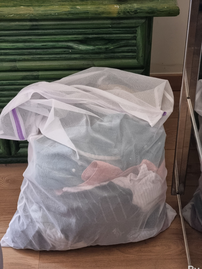 Posé sur le sol, un filet en tissus synthétique de 60cm par 40cm rempli de linge en vrac