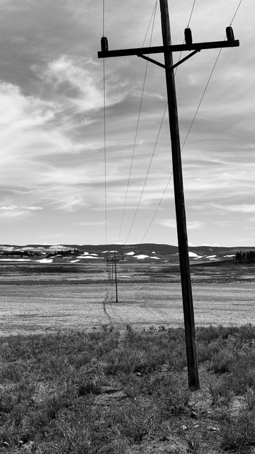 A line of utility poles leads off into a grassy valley. BW