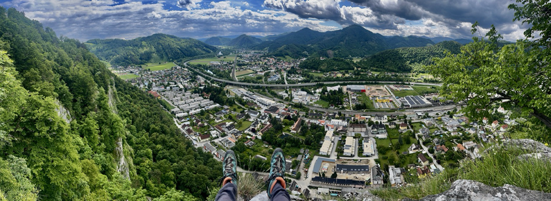 Baumelnde Beine direkt über der Felswand mit Blick auf die Stadt Peggau mit grünen Hügeln rundum