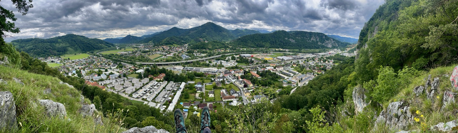 Baumelnde Beine direkt über der Felswand mit Blick auf die Stadt Peggau mit grünen Hügeln rundum