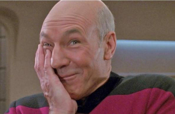 Patrick Stewart as Jean Luc Picard on the bridge of the Enterprise, shoulders hunched, laughing, palm on face.