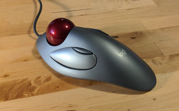 Trackball-Maus mit symmetrischem Design. Links ein großer und ein kleiner Button zu sehen, mittig vorn der große rote Trackball.