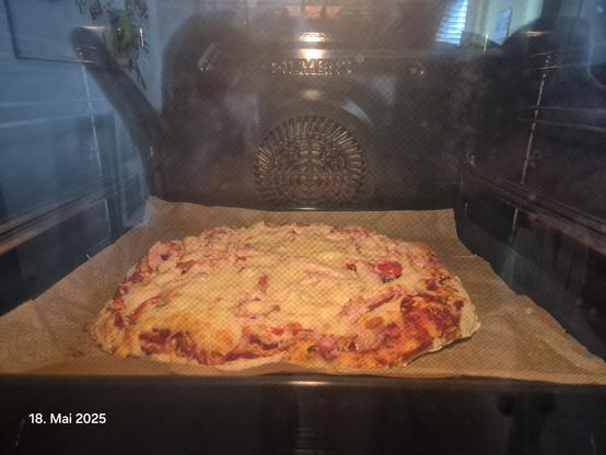 Pizza in einem Ofen. An manchen Stellen haben sich schon knusprige Blasen im Teig gebildet.