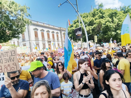 Imagen de una manifestación multitudinaria. La gente porta banderas canarias con las 7 estrellas verdes y diversos carteles.
