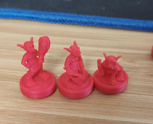 3 monstres de type gobelin sur socle. Imprimer en 3d en filament rouge.lz tout sur un bureau en bois