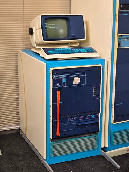 A short rack containing a a Data General microNOVA minicomputer with a Data General Dasher 6053 terminal sitting on top of it displaying a running console.