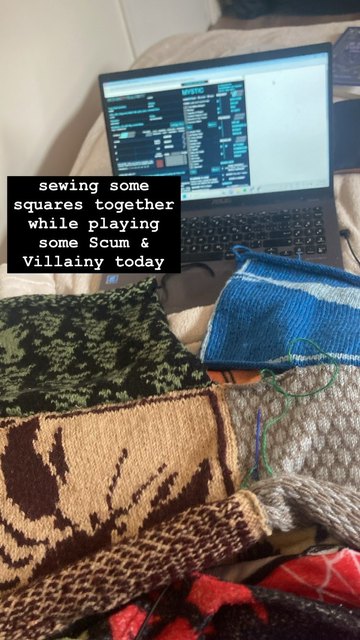 A set of knitted squares being sewn together rests in front of a laptop.
