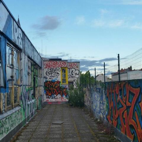 west germany outdoor terrace - 1960s concrete walls and floor, all sprayed over multiple times with graffiti, blue sky above, a few white and grey clouds in there, fluffy.