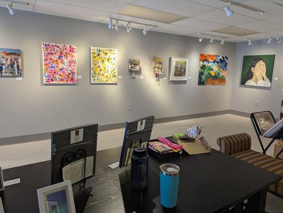 Behind a desk, looking at several colorful 2D works
