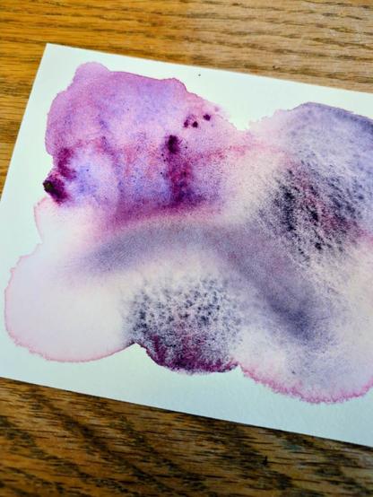 This is a watercolor swatch of Daniel Smith Rose of Ultramarine and Lunar Violet pushed to reveal their granulation. The Rose of Ultramarine leaves a distinct pink edging as it's watered down with bursts of blue splitting out with a few spots of reddish purple masstone.  The lunar violet granulates very gritty and dark and hazy purple.