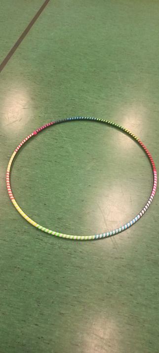 Der Hula Hoop Reifen in Regenbogenfarben liegt auf dem Turnhallenfußboden