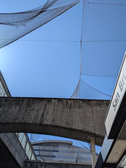 Bird netting overhead above a concrete structure. The bird netting is in poor condition and many parts of it have completely fallen down.