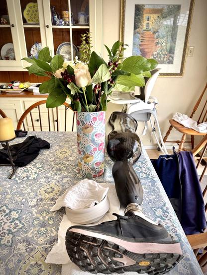 Image of a vase of roses on a dining table next to a bionic leg with tennis shoe on.