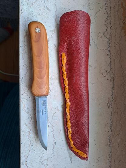 A small wooden handled knife next to a red leather sheath.