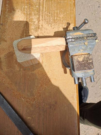 The knife in a vise, the handle is poking out.  Everything is covered in wood shavings, as this is midway through the process of shaping the handle.