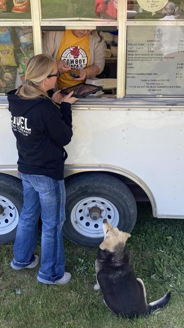 Food truck.  A woman stands by the sliding window of a white food truck and orders her food.  My neighbors’ dog (town dog) sits on the ground looking up expectantly.