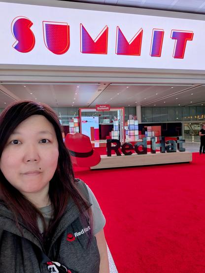 Selfie in front of a large Red Hat sign and the word Summit flashing across the monitors above my head. This is at the Boston Convention and Exhibition center.