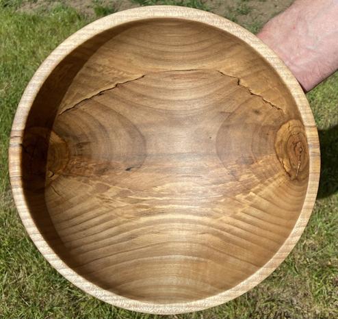 A wooden bowl, seen from above, showing dark grain patterns, and crooked black line, caused by a fungus.