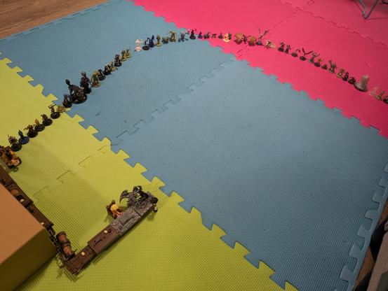 Miniatures from different fantasy tabletop games are lined up in an arc on mats.