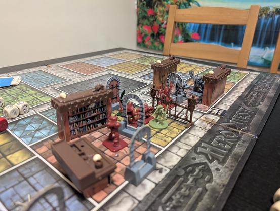 A board for HeroQuest set up for the start of a game. Heroes and monsters can be seen amid furniture.