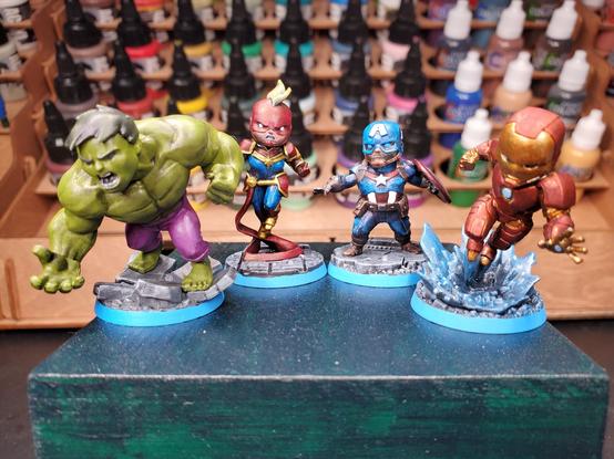 Photo of painted miniature versions of (from left to right) Hulk, Captain Marvel, Captain America (Steve Rogers), and Iron Man sitting atop a green box.