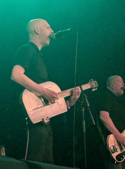 Singer playing guitar in shape of a caravan. Bassist in background