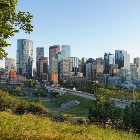 Photograph of a city core in summer, looking down from a green hill and over a bridge.