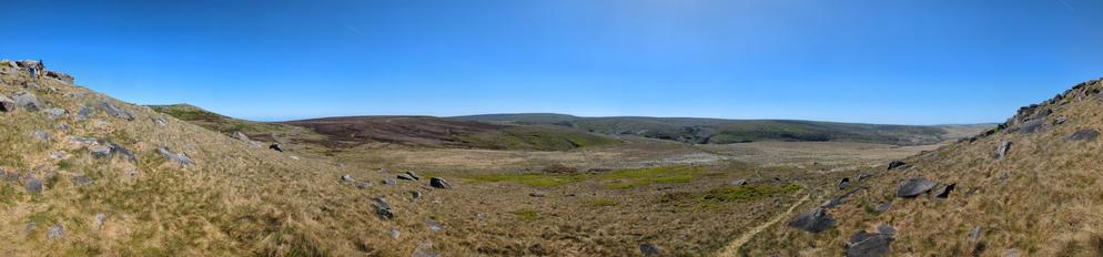 Panorama of hills descending to the bowl of a valley head.   A small reservoir is nestled a ways off.  The path continues up and down from the photographer's standpoint