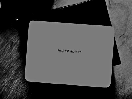 A black-and-white photo of an Oblique Strategy card. The card reads: 'Accept advice'.